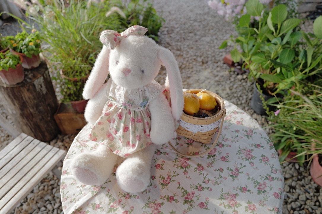 A white rabbit doll beside a basket of fruit in a sunny garden