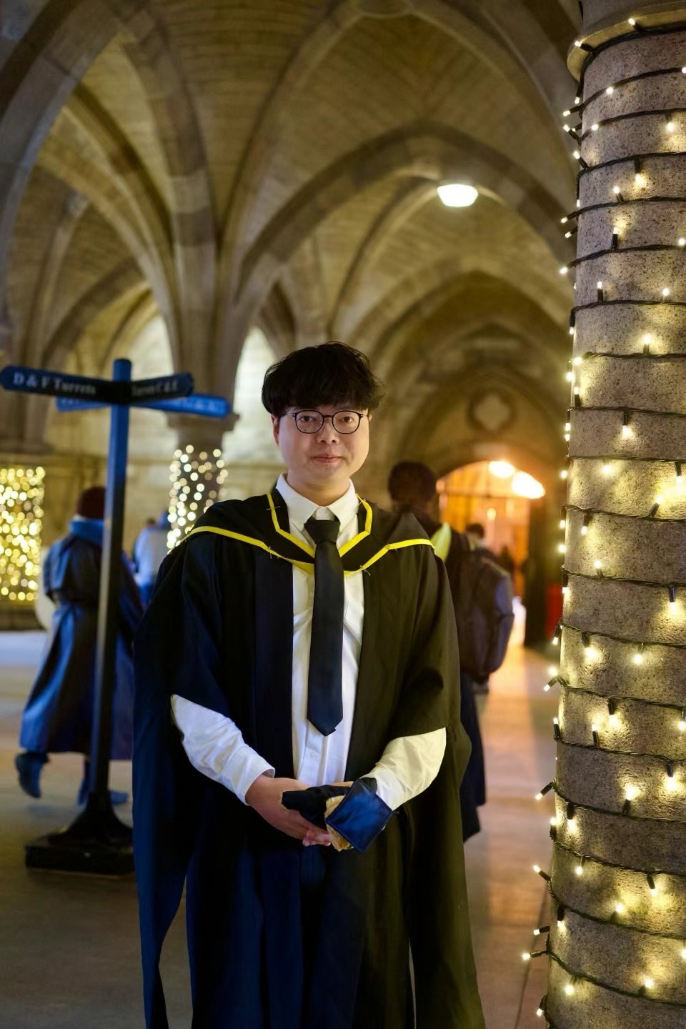 Xinyu Guan in graduation robes beneath stone arches decorated with string lights