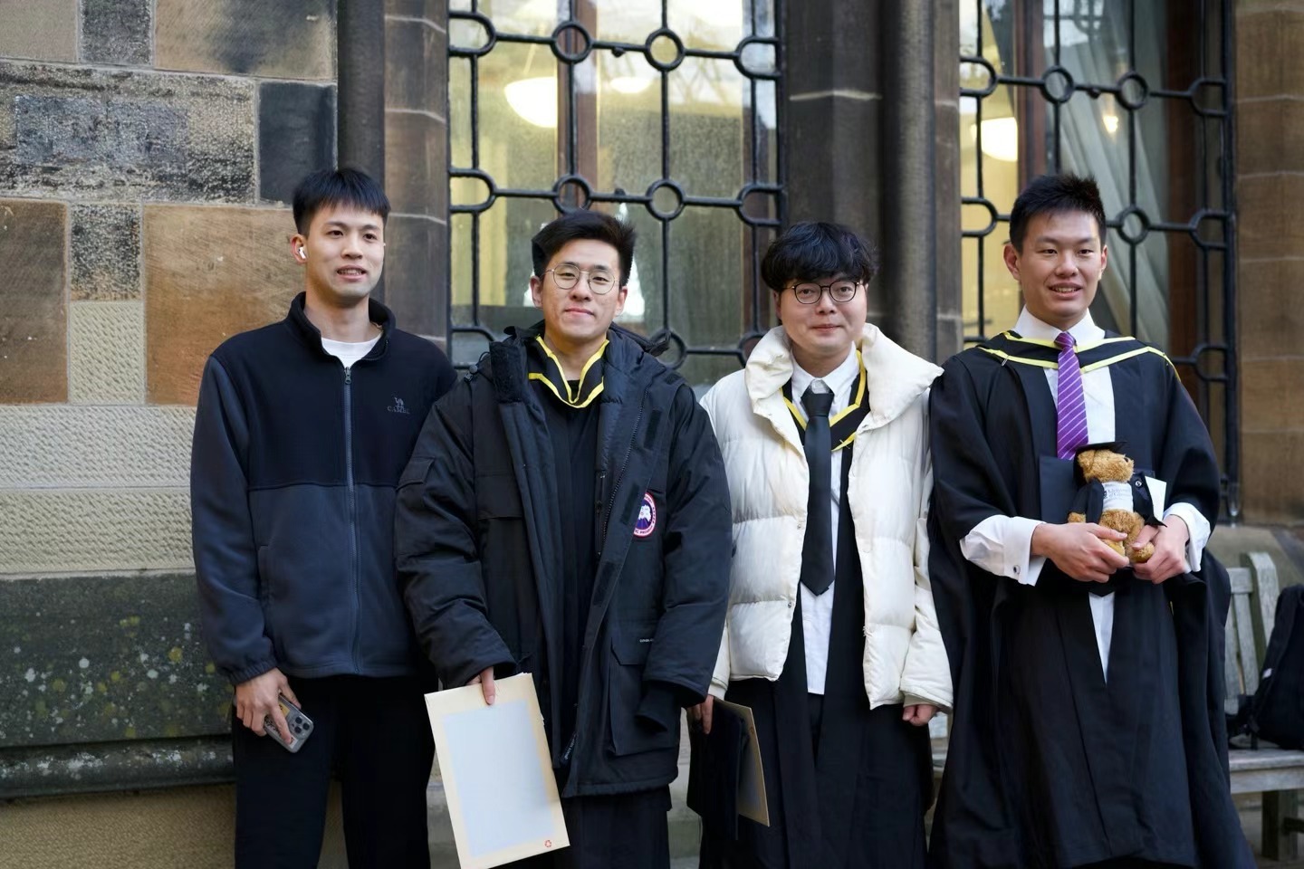 Xinyu Guan with three friends outside a stone university building on graduation day