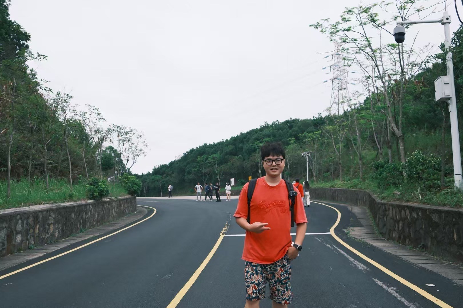 Xinyu Guan in a red shirt walking along a tree-lined road