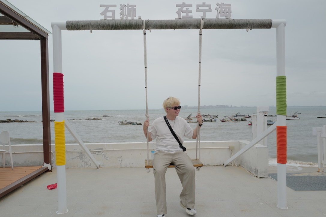 Xinyu Guan sitting on a seaside swing in Ninghai