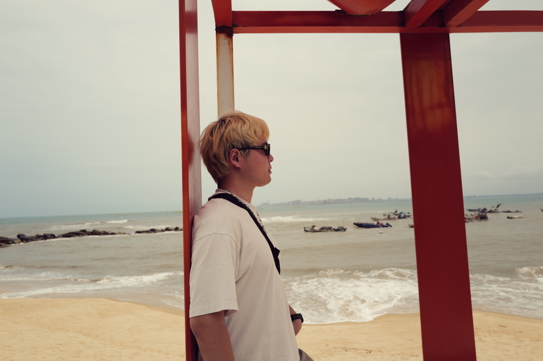 Xinyu Guan looking toward the sea beneath a red pavilion
